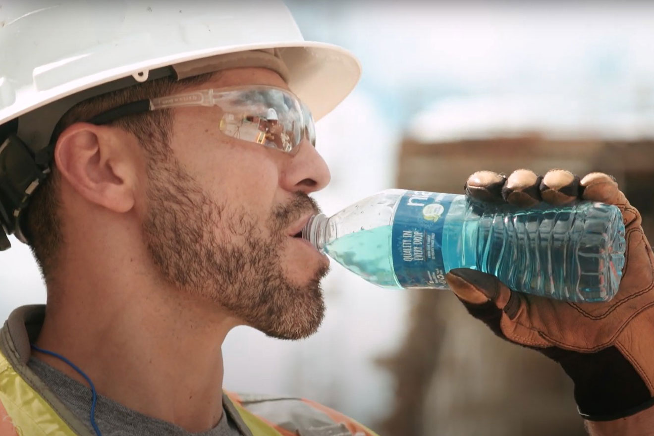 a photo of a worker drinking an Overtime drink mix from a bottle of Niagara water
