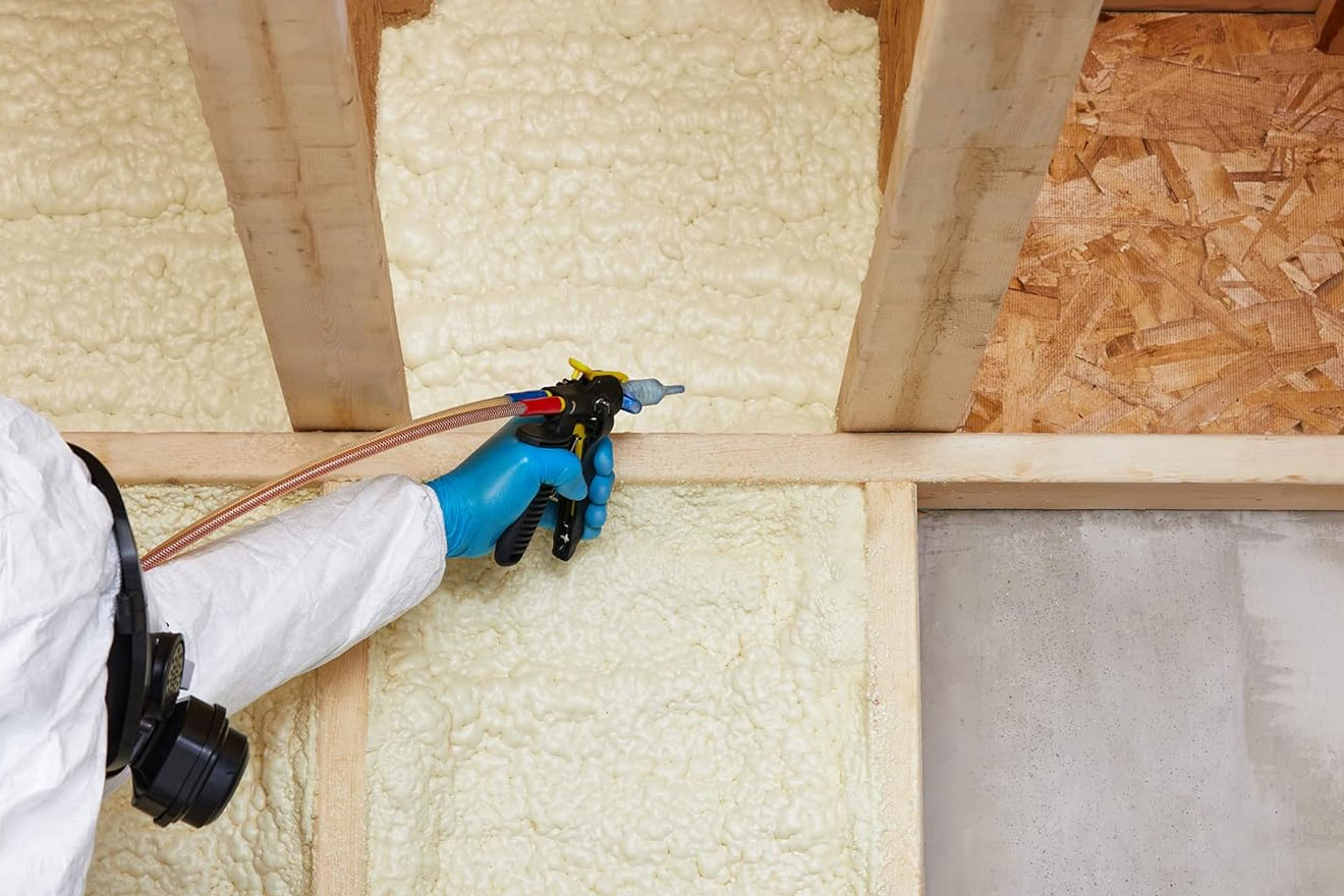 an image showing a person in coveralls applying spray foam insulation to an unfinished house